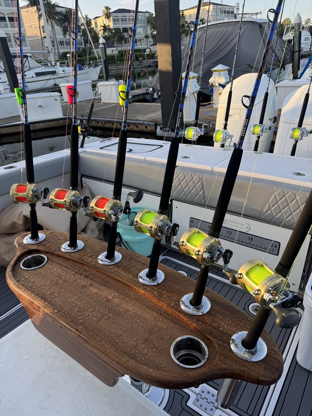 Tiki rods with lever-drag reels standing in a varnished wooden rocket launcher on the back of a boat, a marina behind