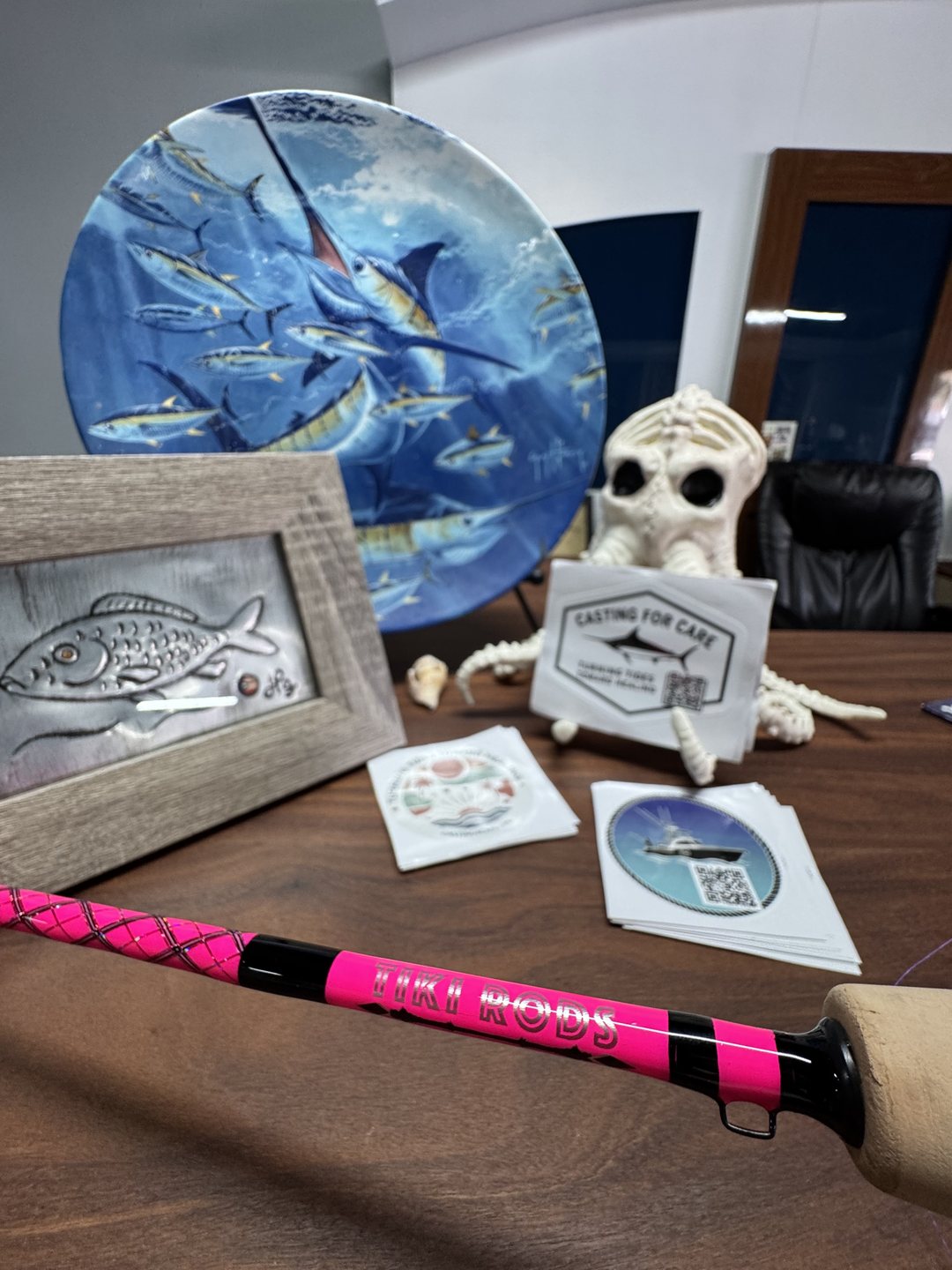 The pink Casting for Care rod standing against a desk of marlin artwork and foundation cards