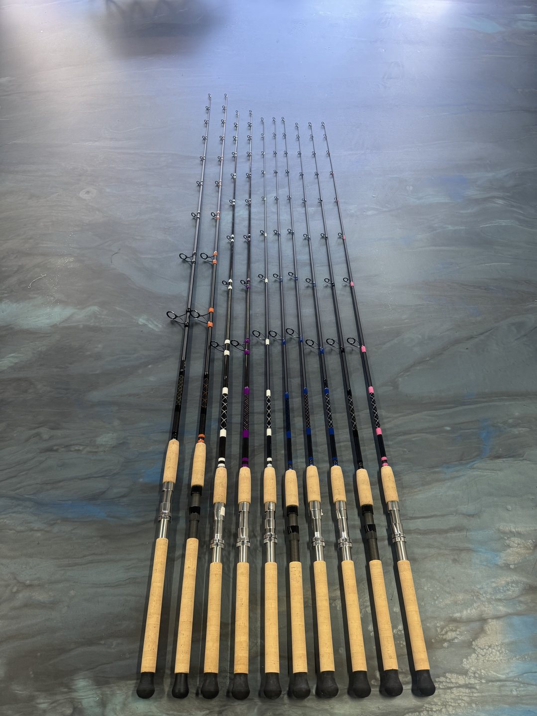 A set of ten rods fanned across the marbled bench, cork foregrips above black butt sections