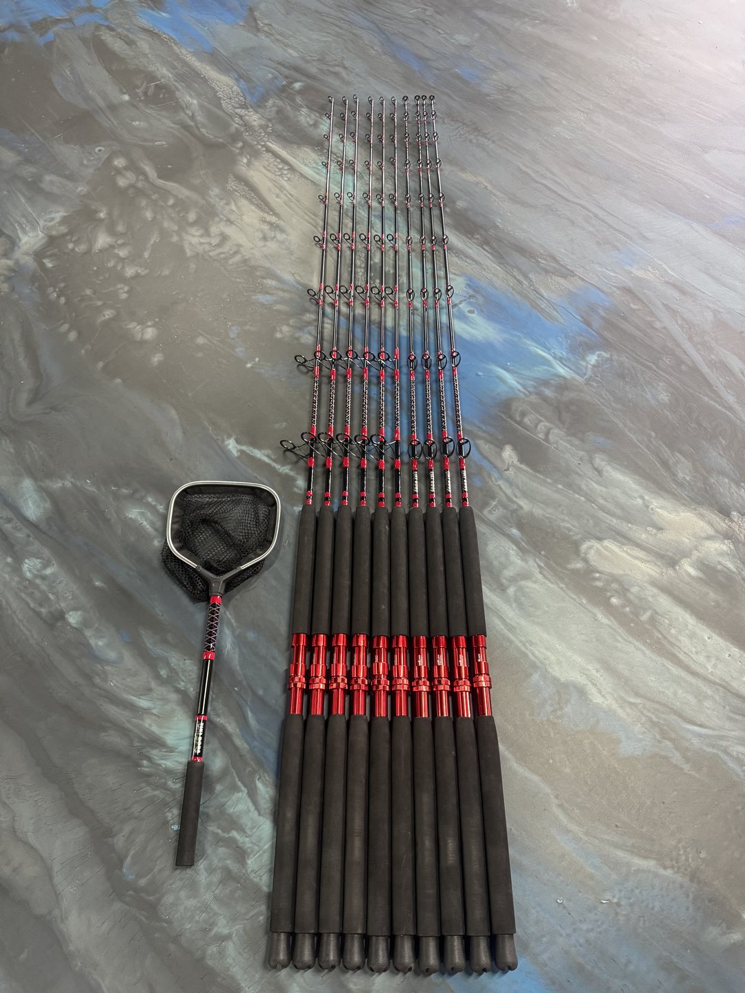 A set of rods wrapped in red thread laid out with a landing net on the marbled bench