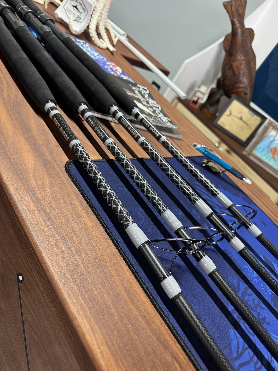 Finished rods resting on the shop counter, a carved fish sculpture and framed artwork on the wall behind