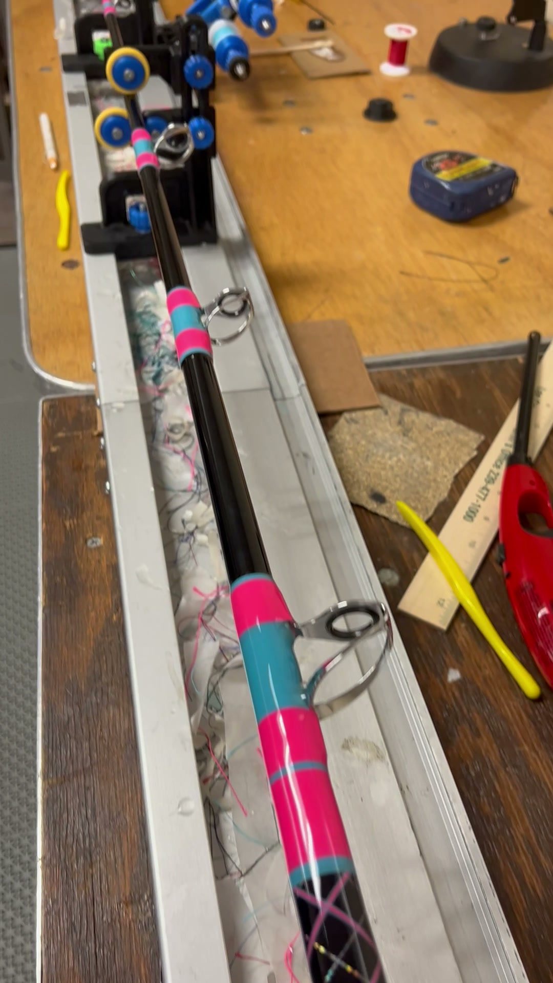 A blank on the wrapper, pink and teal thread already laid over the guide feet, spools and tools on the bench behind